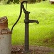 gammal brunn med pumphandtag och en mjölkkanna